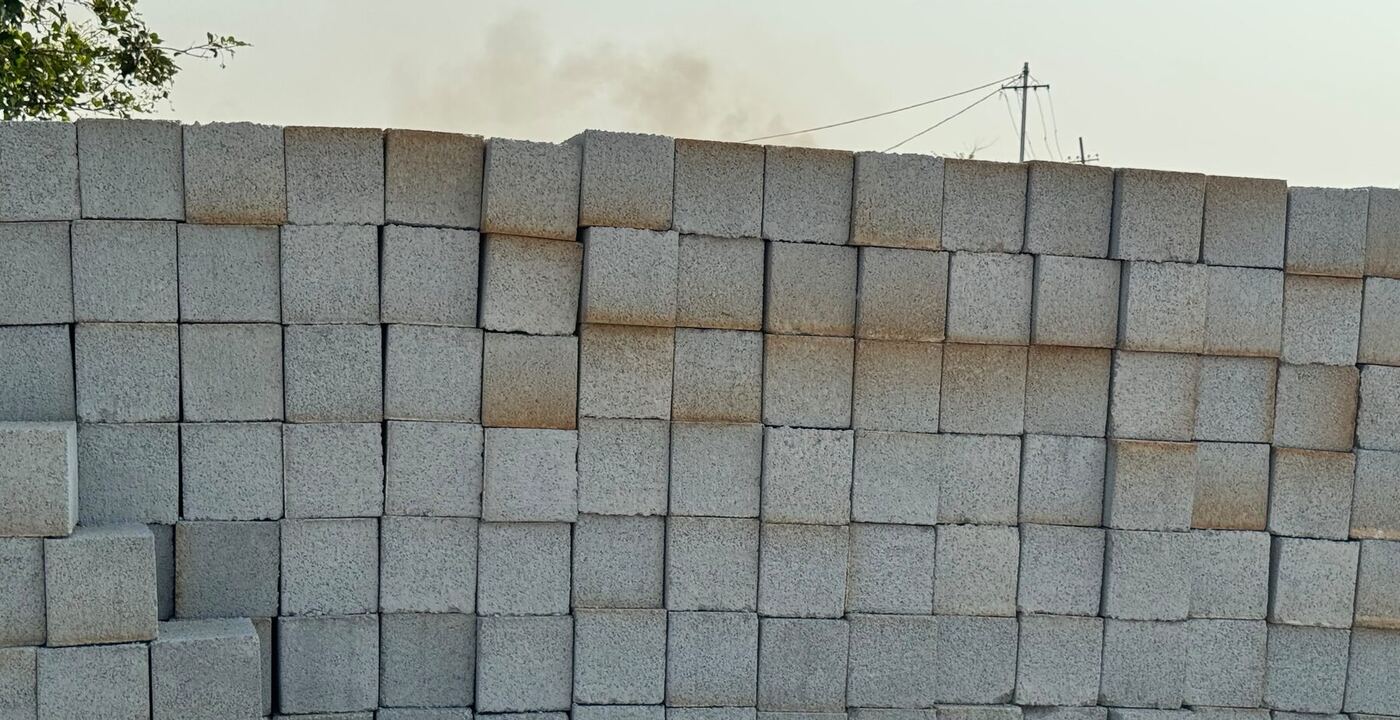 A long wall of stacked grey concrete blocks at the Supreme Brick Factory yard