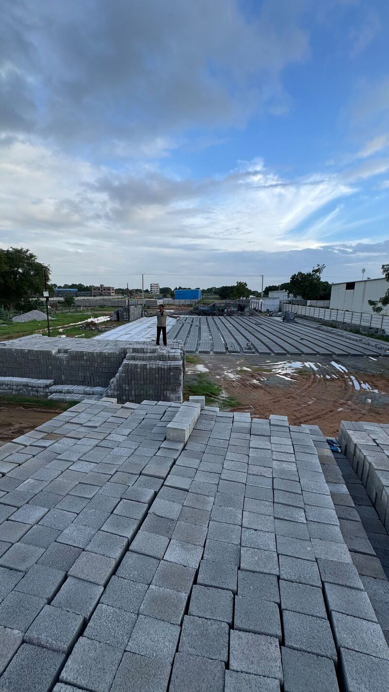 A worker standing on a stack of concrete blocks with thousands more curing in rows across the Supreme Brick Factory yard